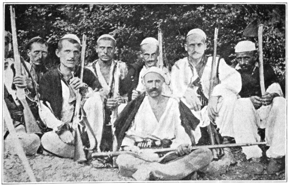 eight men, seated in native dress, all holding firearms